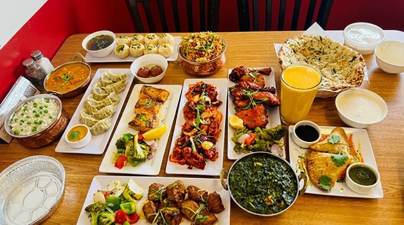 A table laden with a variety of colorful Indian and Nepalese dishes, including curries, momos, and naan.