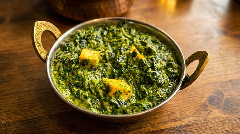 Palak Paneer, a vibrant green spinach and cheese curry, served in a traditional brass bowl.